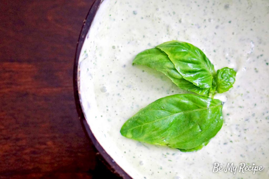 Lemon basil aioli sauce in a coconut bowl, decorated with fresh basil leaves.