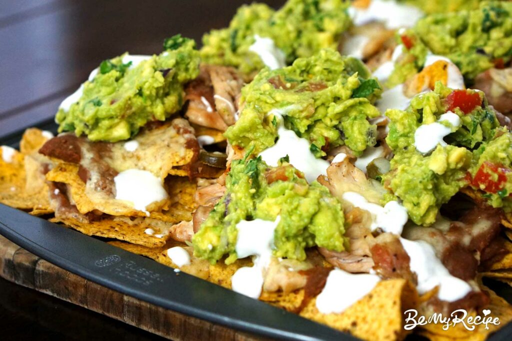 Loaded nachos with refried beans, cheese, chicken, jalapenos, cilantro, guacamole, and sour cream