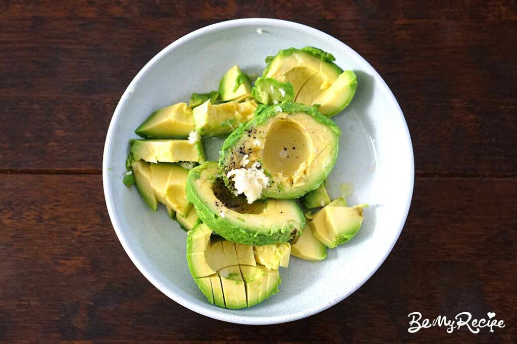 Scooped up avocado with minced garlic, salt, pepper, and lime juice in a bowl.