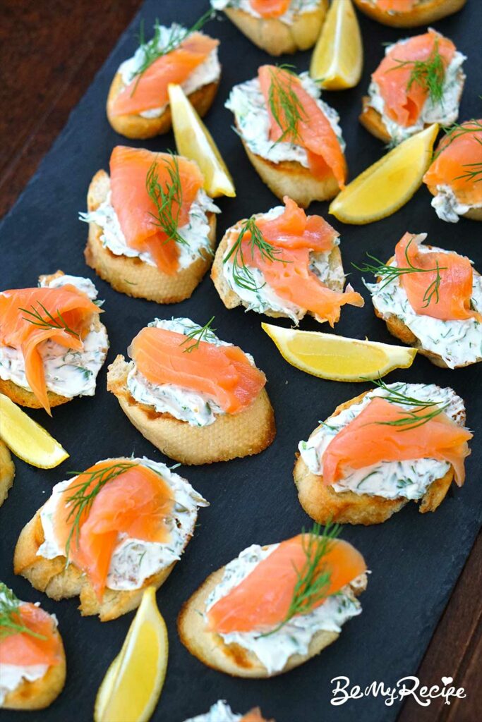 Smoked salmon crostini on a board with lemon wedges