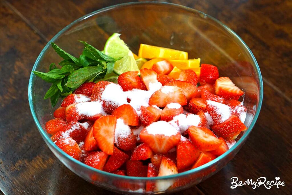 Mixing the chopped strawberries, lime, orange, mint, and sugar in a bowl.