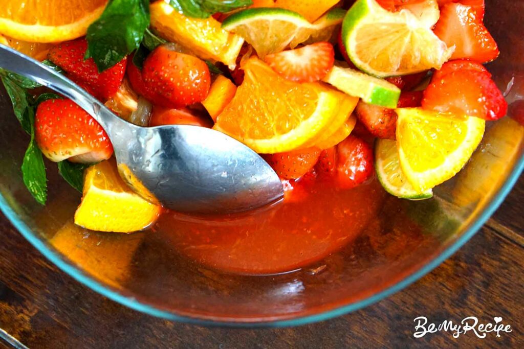Juices from the chopped strawberries, lime, orange, mint, and sugar in a bowl.