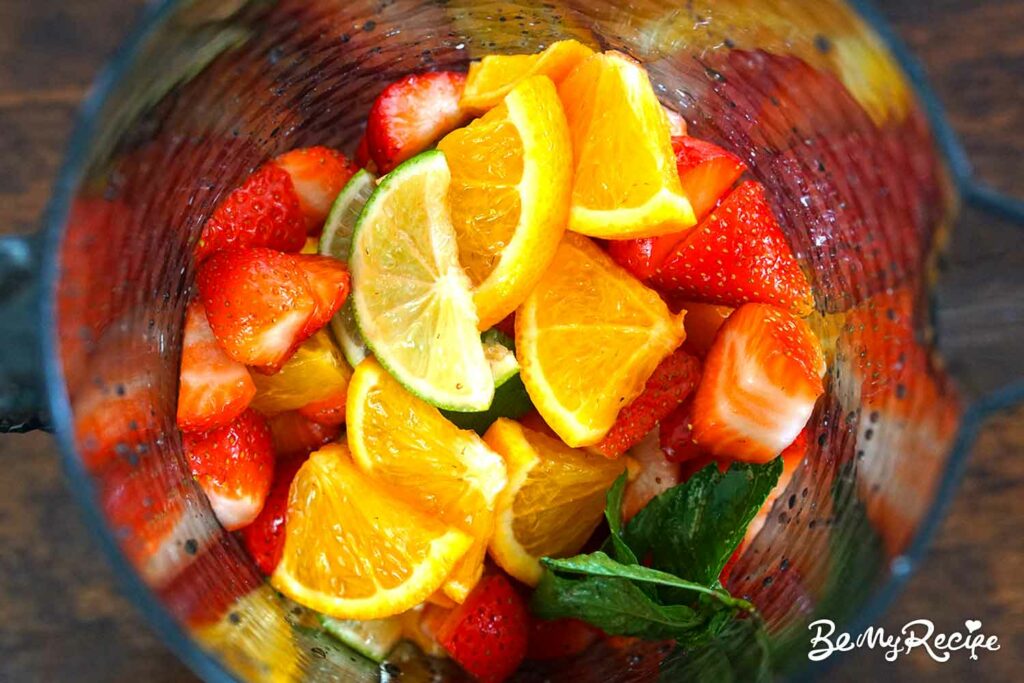 Chopped strawberries, lime, orange, mint, and sugar in a pitcher.