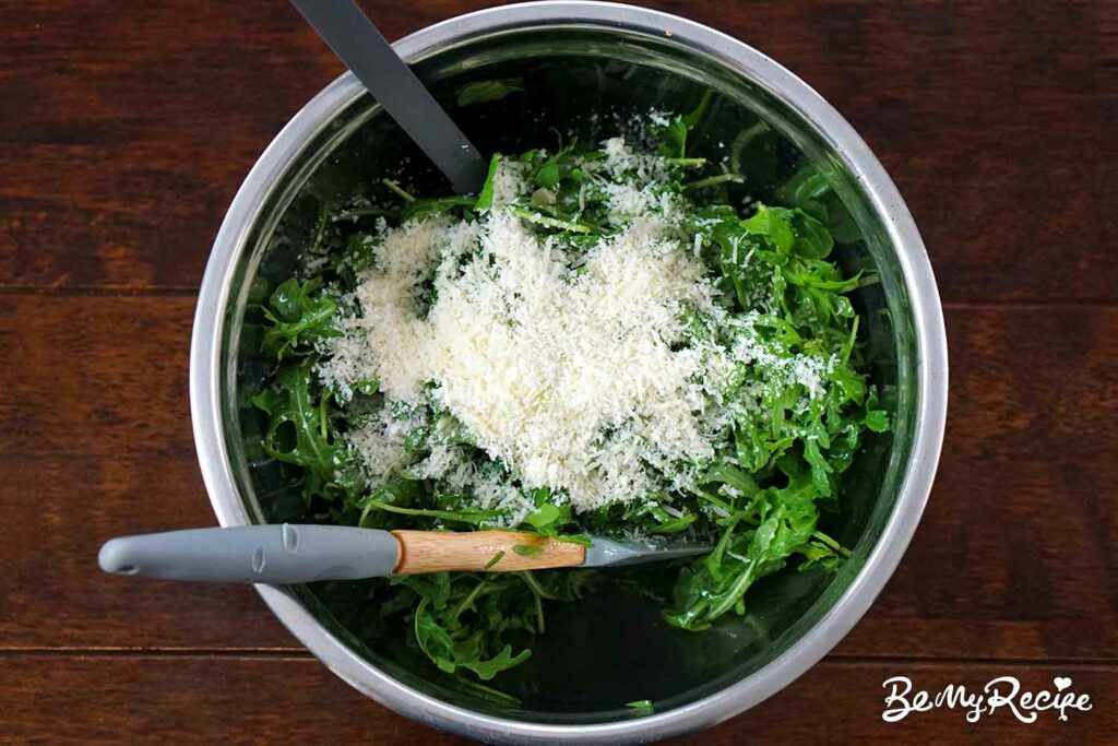Adding the grated parmesan to the arugula.