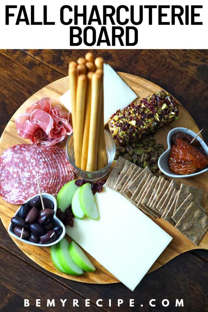 Charcuterie board that includes a Goat Cheese Log, Gruyere Cheese, Ossau-Iraty Cheese, Salami, Prosciutto, Sourdough crackers, Breadsticks, Kalamata Olives, Sundried Tomatoes, Apples, Pistachios, and Cranberries.