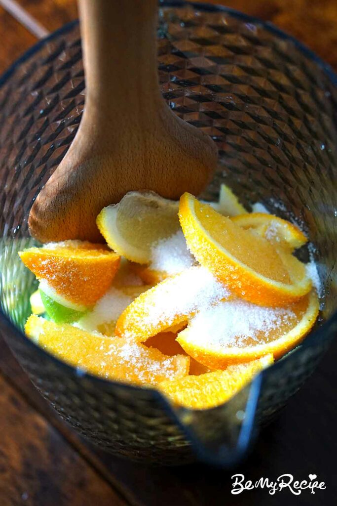 Sliced fruit and sugar in a pitcher (pressing lightly with a wooden spoon to release some of the citrus juice)