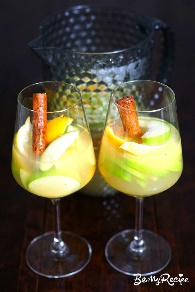 Apple Cider Sangria with Oranges, Lemons, and Cinnamon in two glasses and a pitcher