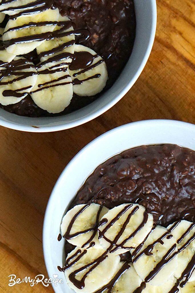 Banana hazelnut chocolate oatmeal in bowls topped with banana slices and melted chocolate.