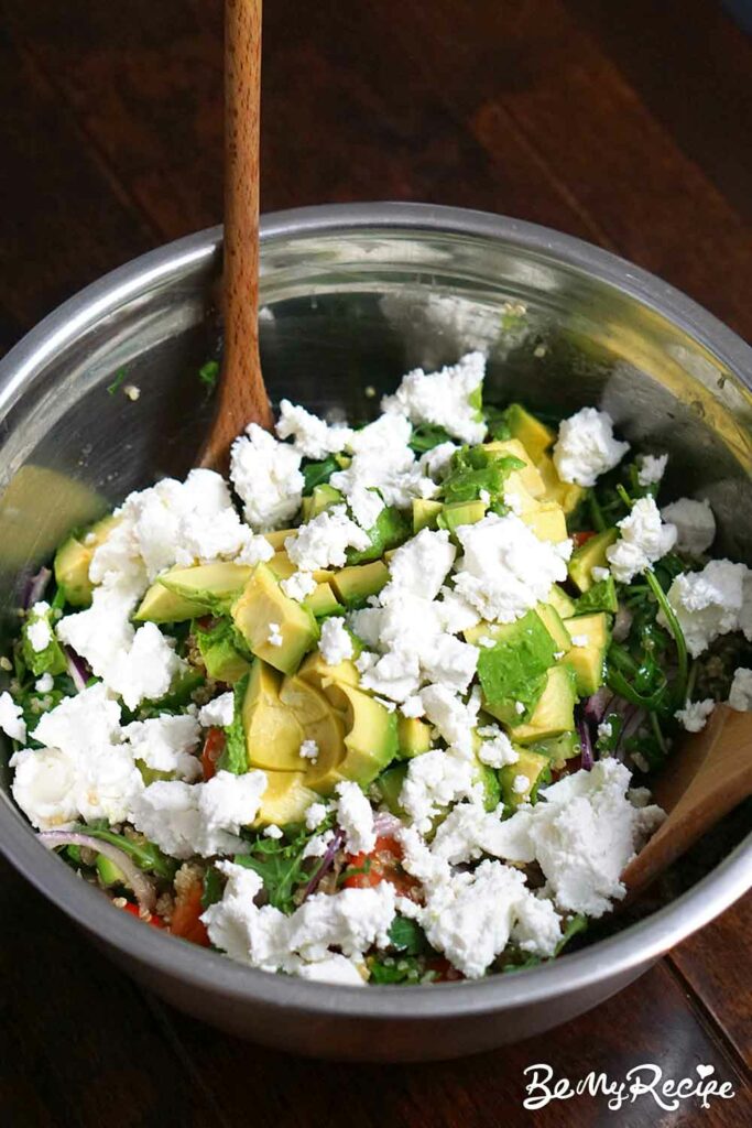Adding the chopped avocado and crumbled soft goat cheese to the quinoa salad.