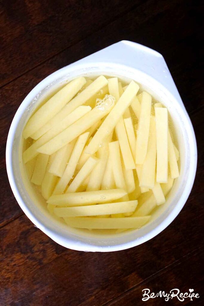 overhead view of matchstick peel potatoes soaking in cold water in a round white bowl