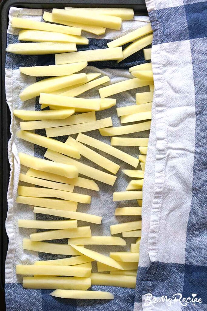 matchstick potatoes that have been soaked in water being patted down with a checkered tea towel