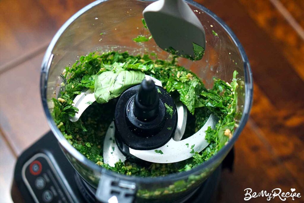 Chopping the basil and nuts in the food processor and scraping the sides.