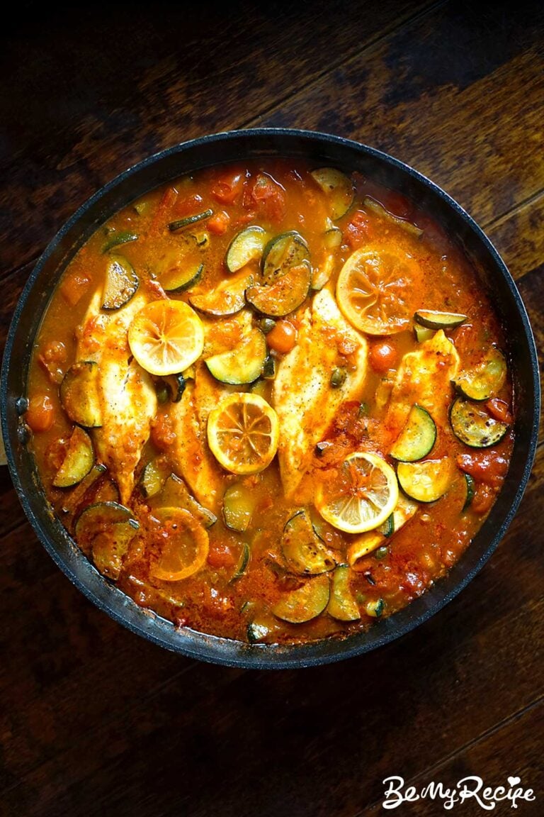 overhead view of one-pan tilapia in prosecco tomato sauce with zucchini served on a dark wooden dining table
